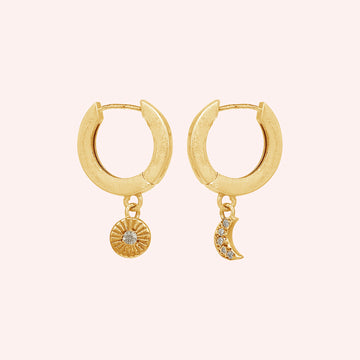 Silver_hoop_earrings_in_gold_plated_silver_with_sun_and_moon_charms_at_front_angle_view_on_solid_pink_background