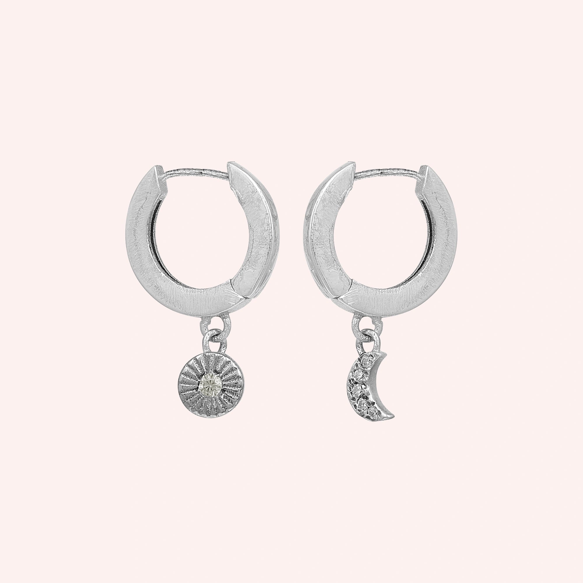 Silver_hoop_earrings_in_sterling_silver_with_sun_and_moon_charms_at_front_angle_view_on_solid_pink_background