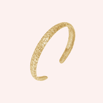 Adjustable_bangle_in_gold_plated_silver_with_a_textured_design_band_at_slight_angle_view_on_solid_pink_background