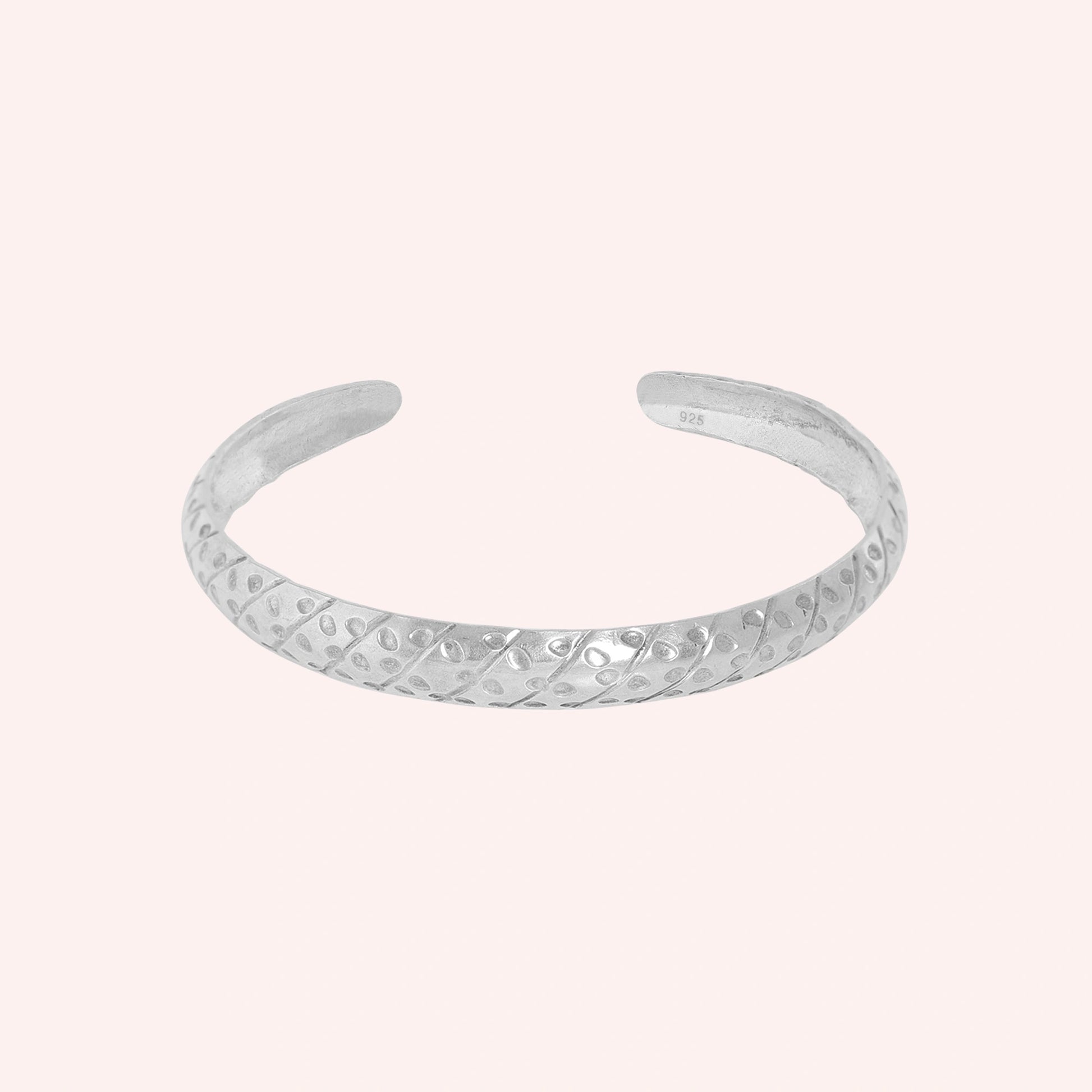 Adjustable_bangle_in_sterling_silver_with_a_textured_design_band_at_front_angle_view_on_solid_pink_background