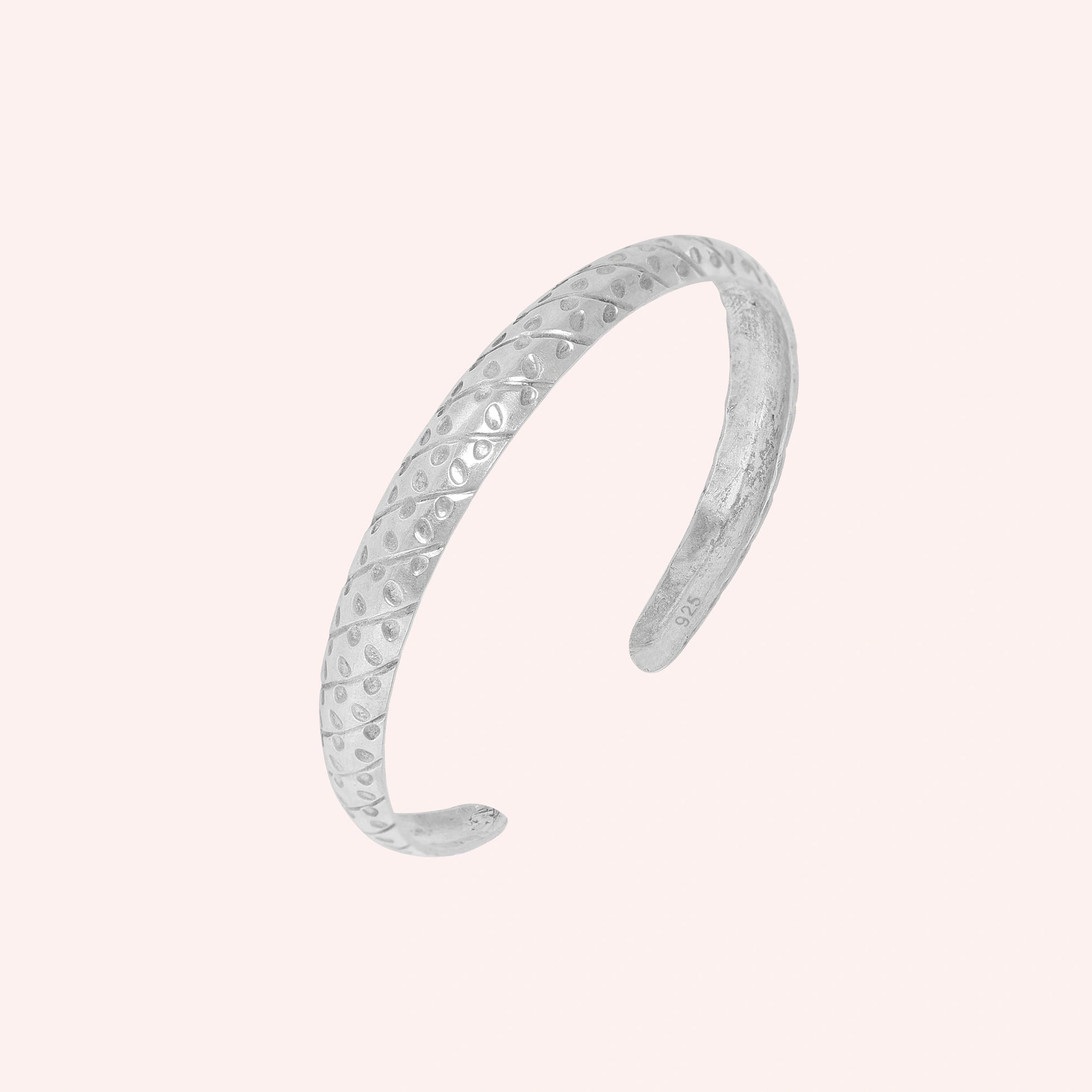 Adjustable_bangle_in_sterling_silver_with_a_textured_design_band_at_slight_angle_view_on_solid_pink_background