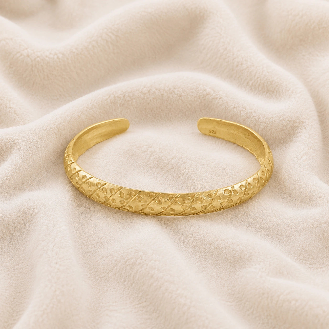 Adjustable_bangle_in_gold_plated_silver_with_a_textured_design_band_at_front_angle_view_on_soft_fabric_background