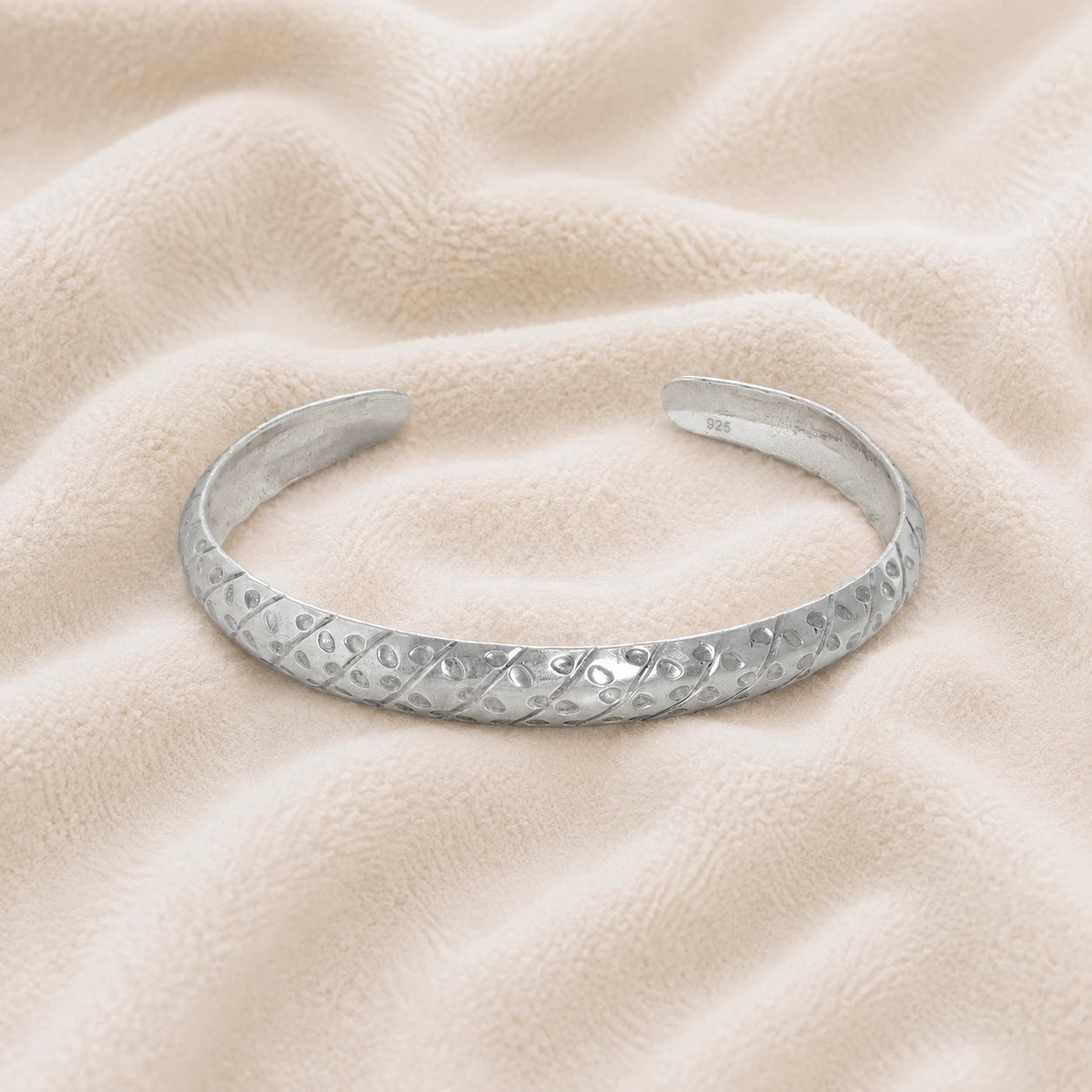 Adjustable_bangle_in_sterling_silver_with_a_textured_design_band_at_front_angle_view_on_soft_fabric_background