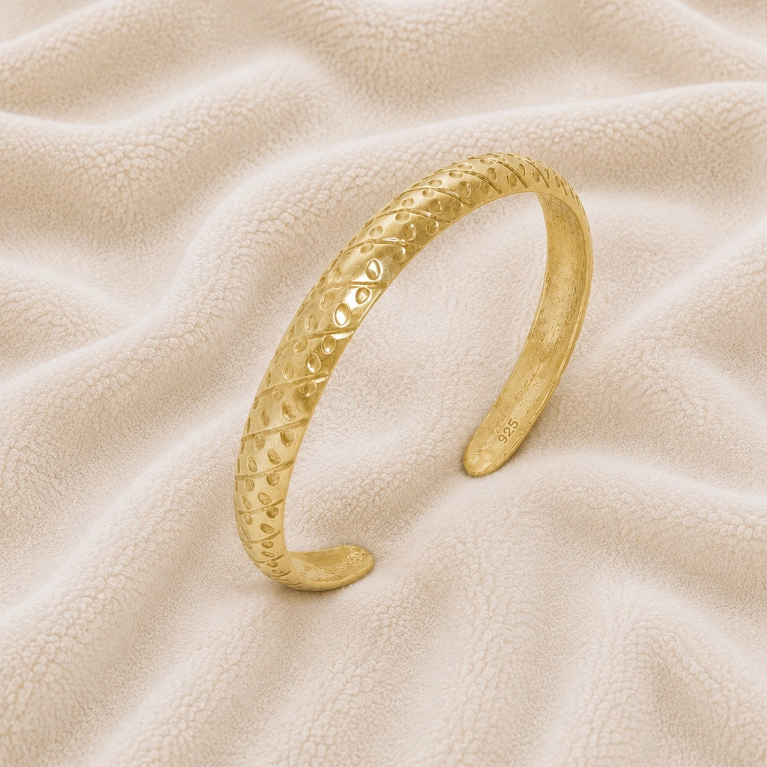 Adjustable_bangle_in_gold_plated_silver_with_a_textured_design_band_at_slight_angle_view_on_soft_fabric_background