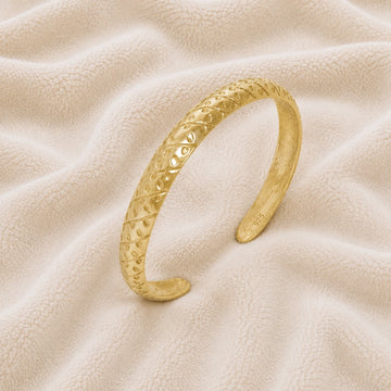 Adjustable_bangle_in_gold_plated_silver_with_a_textured_design_band_at_slight_angle_view_on_soft_fabric_background