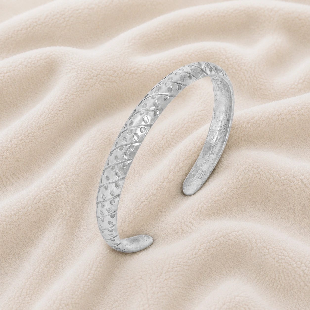 Adjustable_bangle_in_sterling_silver_with_a_textured_design_band_at_slight_angle_view_on_soft_fabric_background
