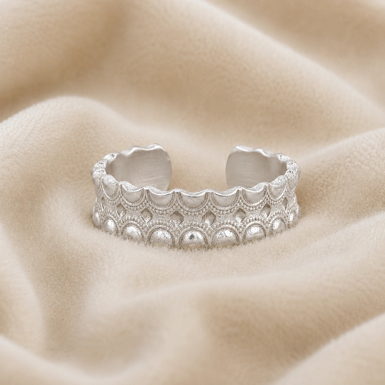 Adjustable_ring_in_sterling_silver_with_handcrafted_deisgn_at_front_angle_on_soft_fabric_background