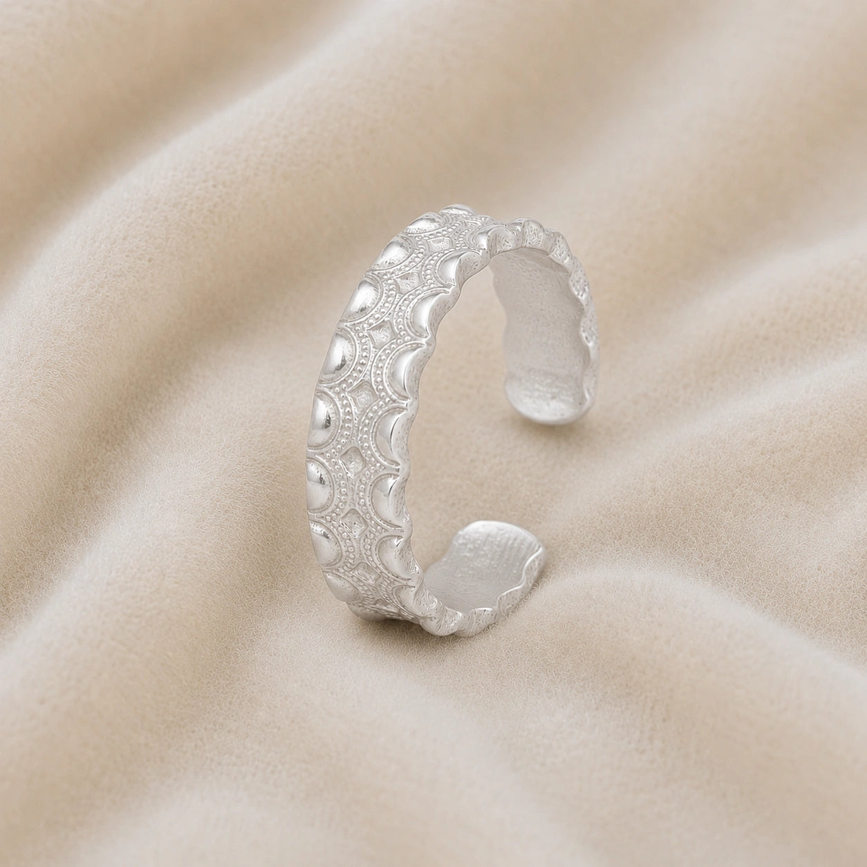 Adjustable_ring_in_sterling_silver_with_handcrafted_deisgn_at_slight_angle_on_soft_fabric_background