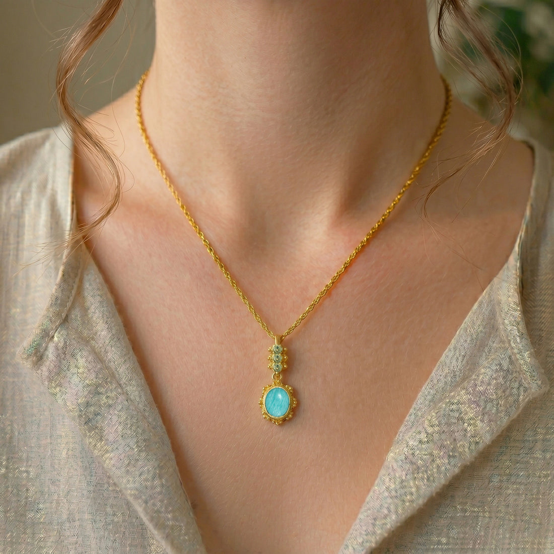 Amazonite_necklace_with_oval_blue_green_stone_gold_plated_silver_pendant_shown_in_slightly_angled_view_on_soft_fabric_background