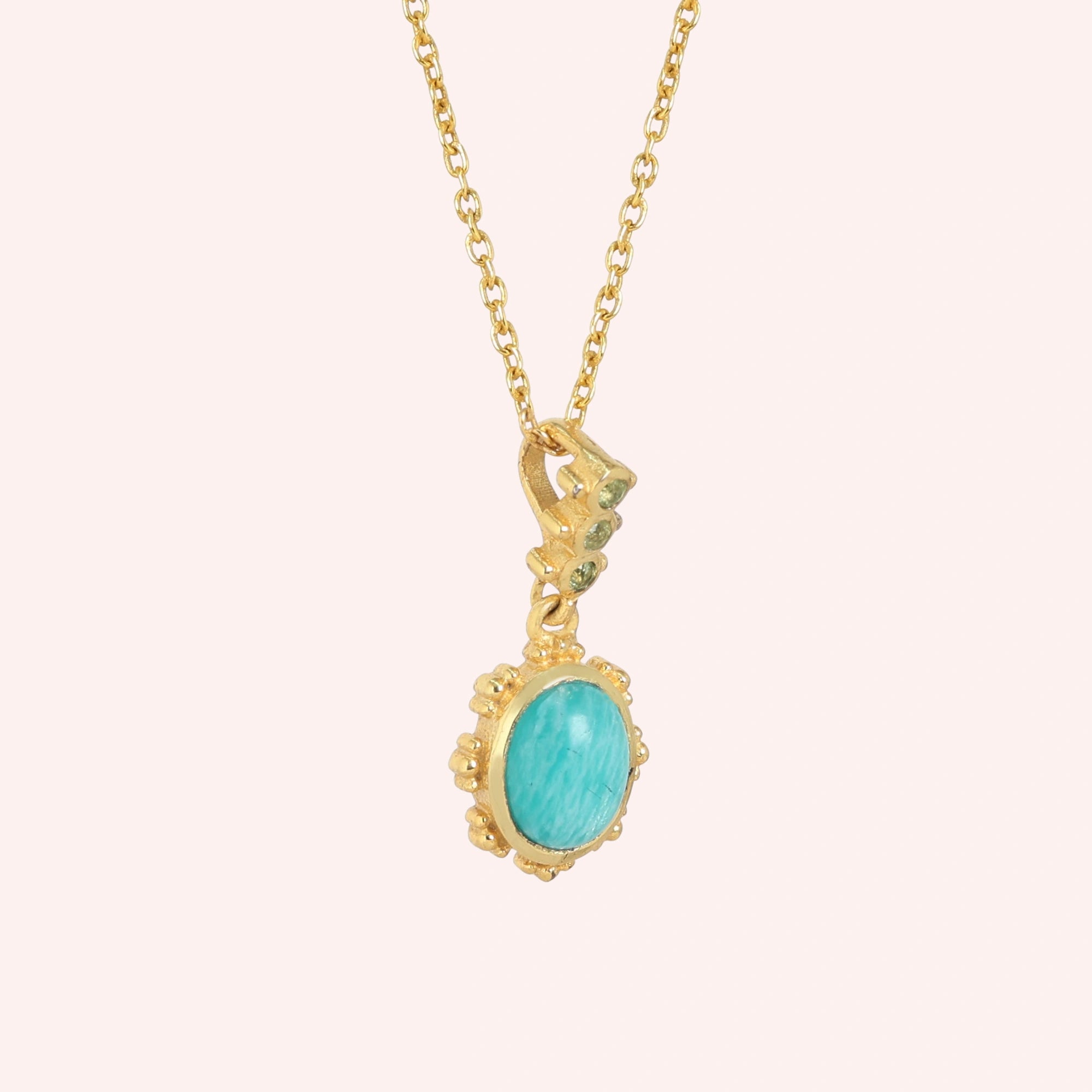 Amazonite_necklace_with_oval_blue_green_stone_gold_plated_silver_pendant_shown_in_slightly_angled_view_on_solid_pink_background