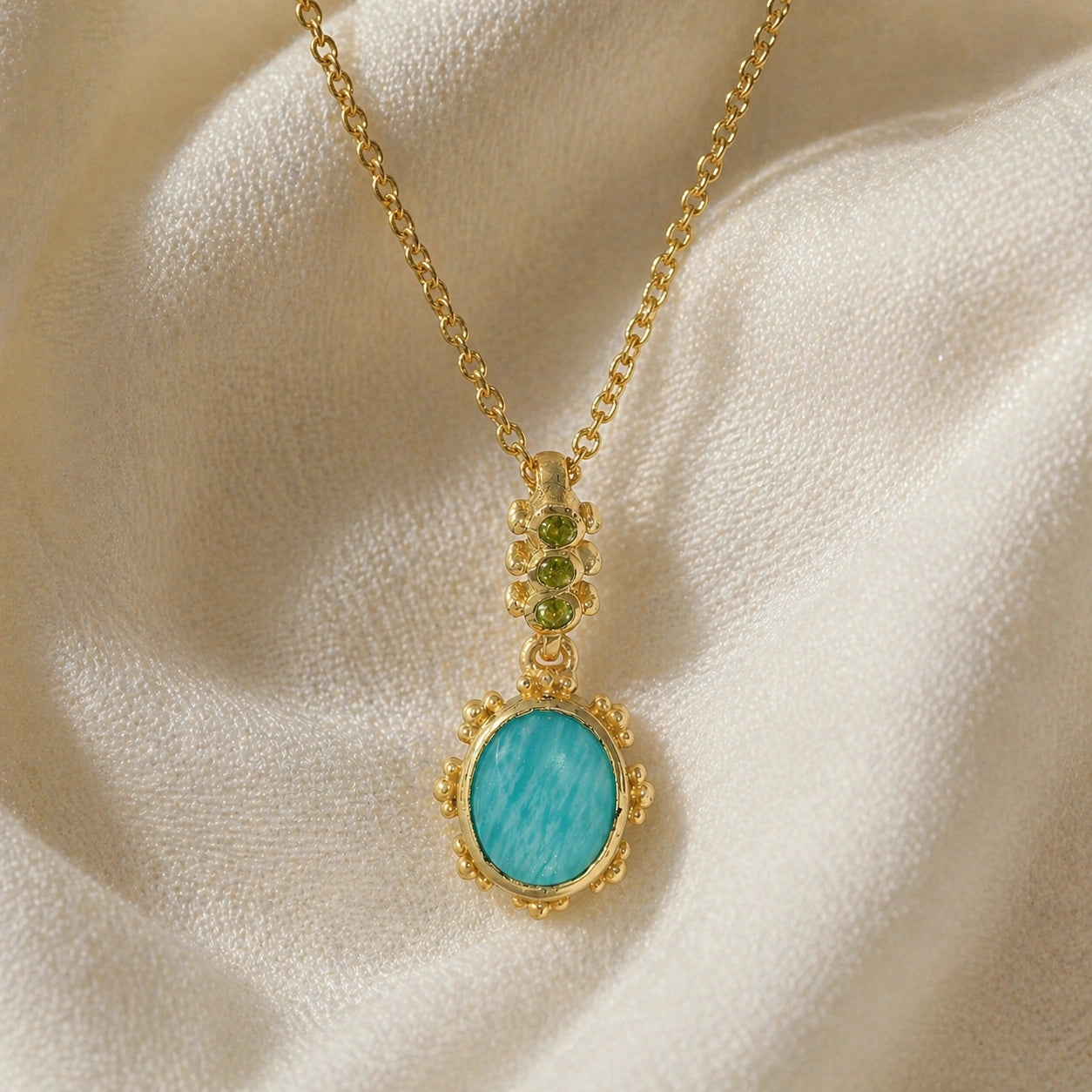 Amazonite_necklace_with_oval_blue_green_stone_gold_plated_silver_pendant_shown_in_front_angled_view_on_soft_fabric_background