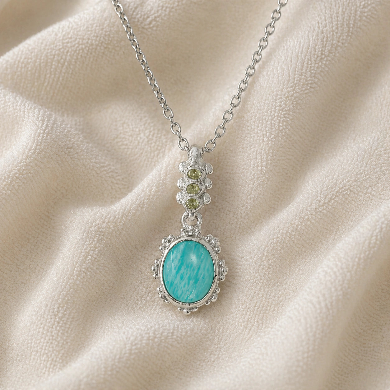 Amazonite_necklace_with_oval_blue_green_stone_sterling_silver_pendant_shown_in_front_angled_view_on_soft_fabric_background