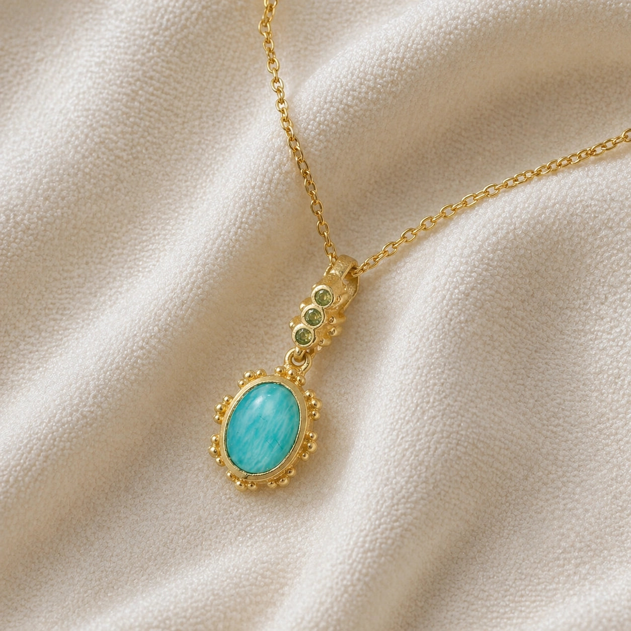 Amazonite_necklace_with_oval_blue_green_stone_gold_plated_silver_pendant_shown_in_slightly_angled_view_on_soft_fabric_background