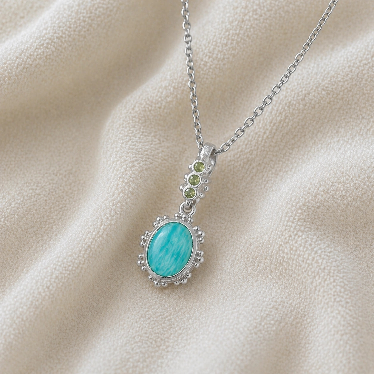 Amazonite_necklace_with_oval_blue_green_stone_sterling_silver_pendant_shown_in_slightly_angled_view_on_soft_fabric_background