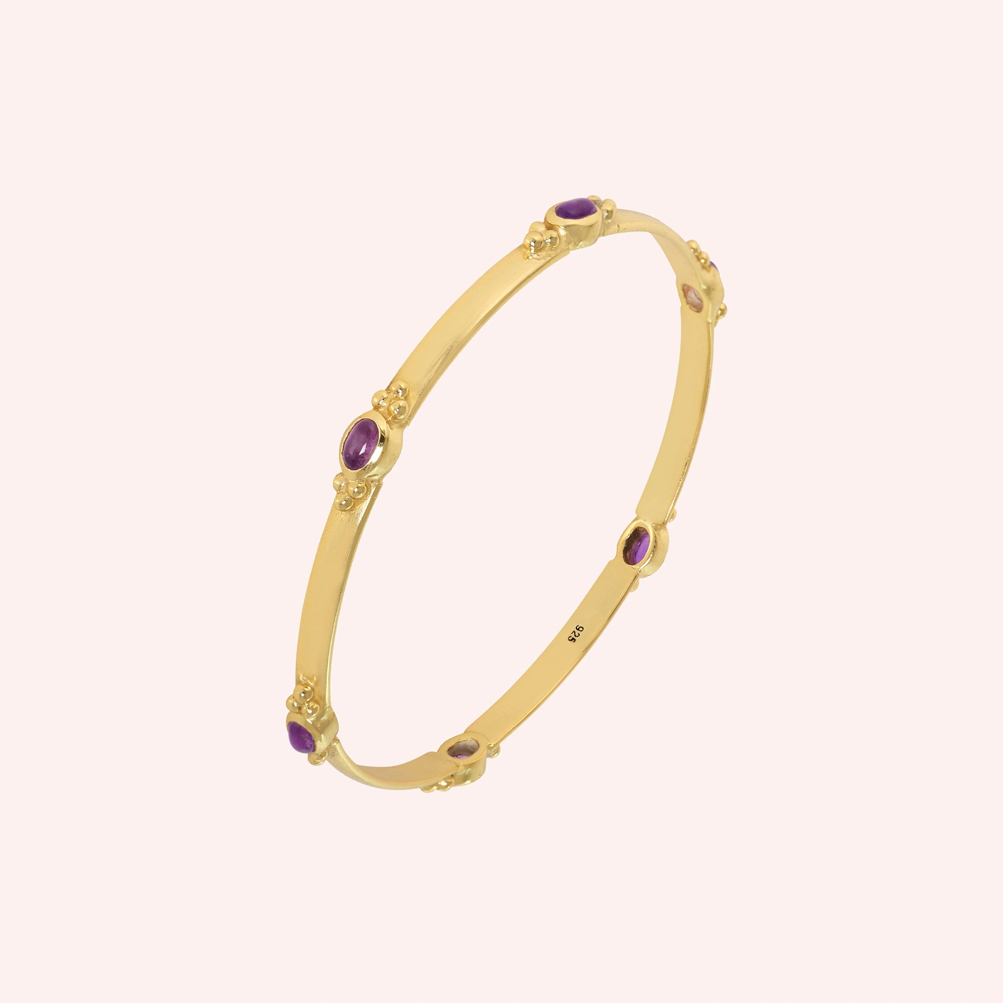 Amethyst_bracelet_in_gold_plated_silver_with_oval_amethyst_stones_at_slight_angle_view_on_solid_pink_background