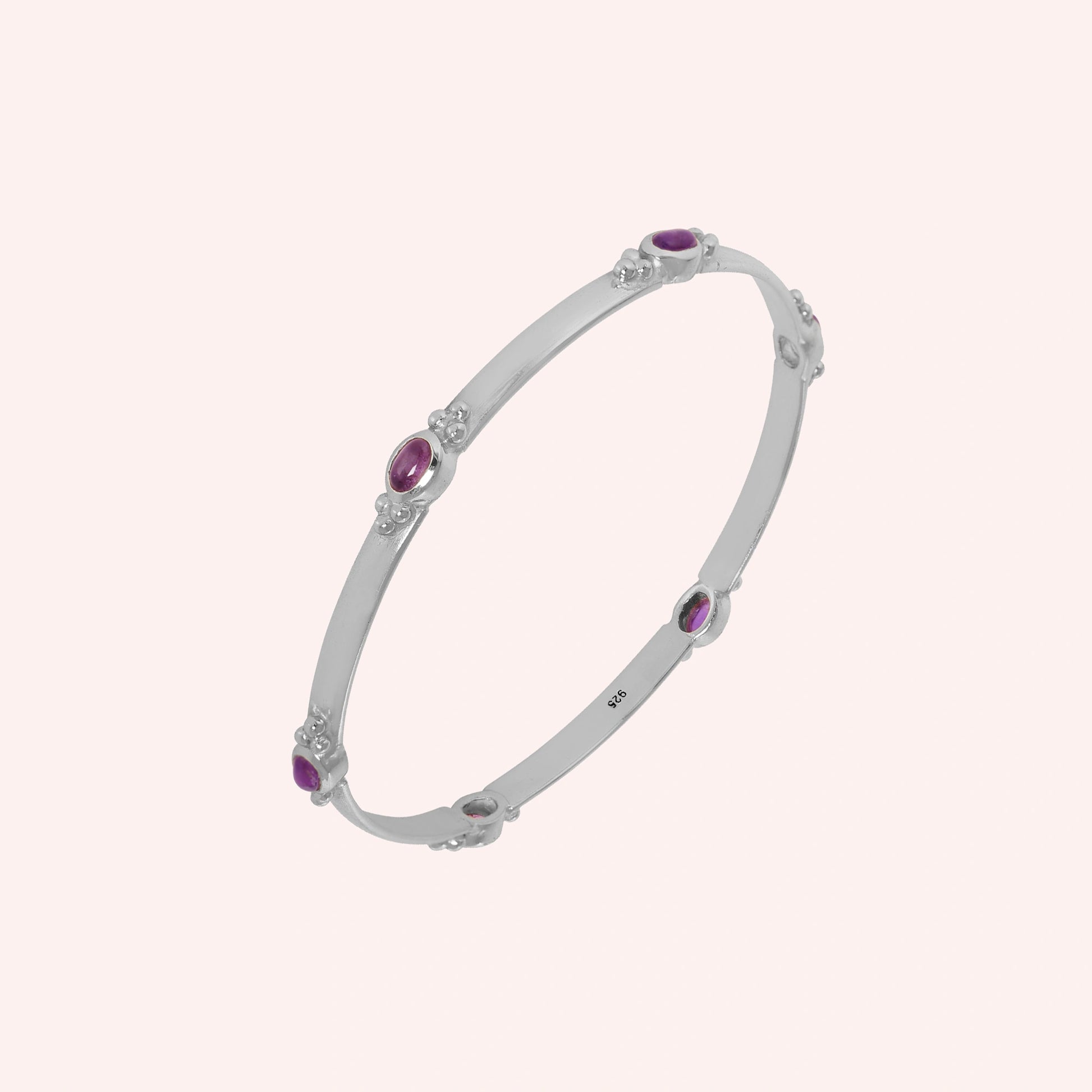 Amethyst_bracelet_in_sterling_silver_with_oval_amethyst_stones_at_slight_angle_view_on_solid_pink_background