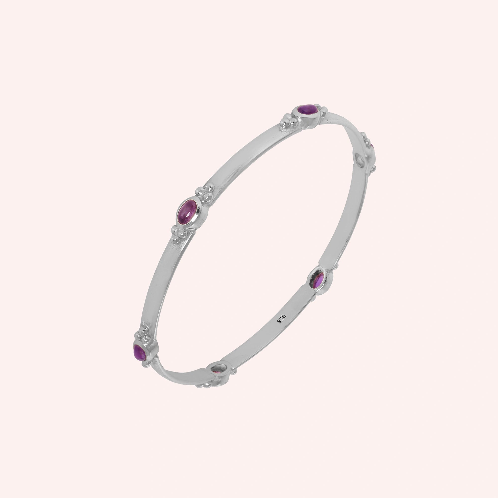 Amethyst_bracelet_in_sterling_silver_with_oval_amethyst_stones_at_slight_angle_view_on_solid_pink_background