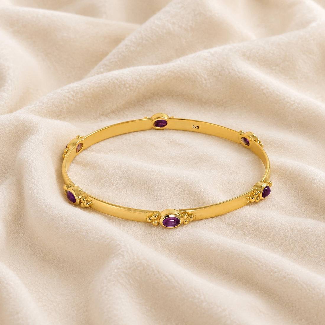 Amethyst_bracelet_in_gold_plated_silver_with_oval_amethyst_stones_at_front_angle_view_on_soft_fabric_background