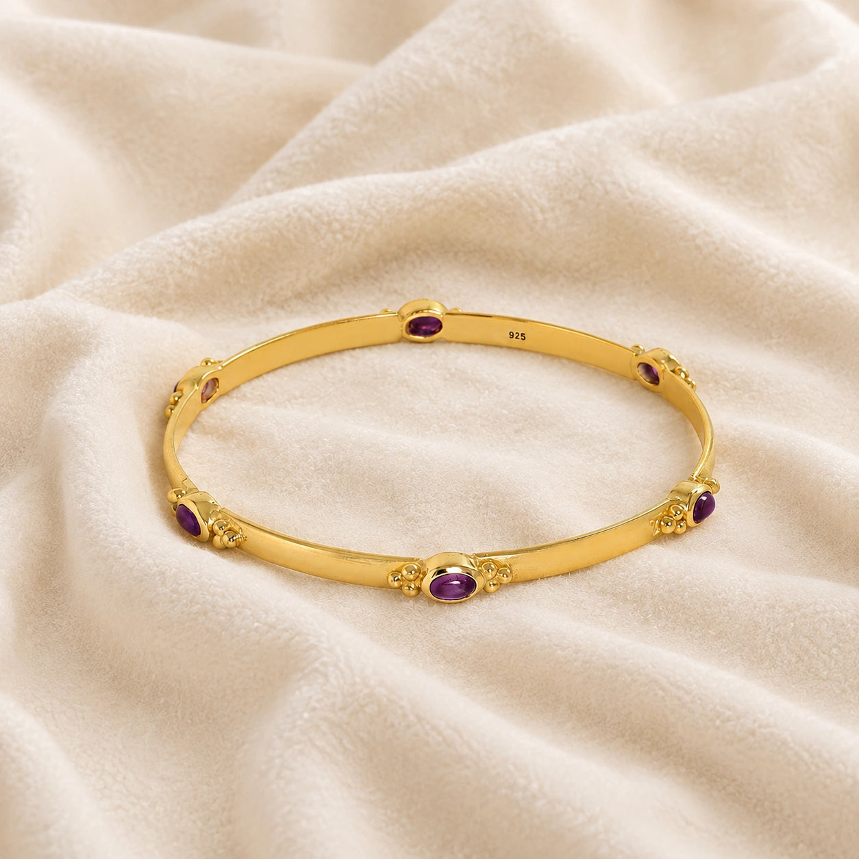 Amethyst_bracelet_in_gold_plated_silver_with_oval_amethyst_stones_at_front_angle_view_on_soft_fabric_background