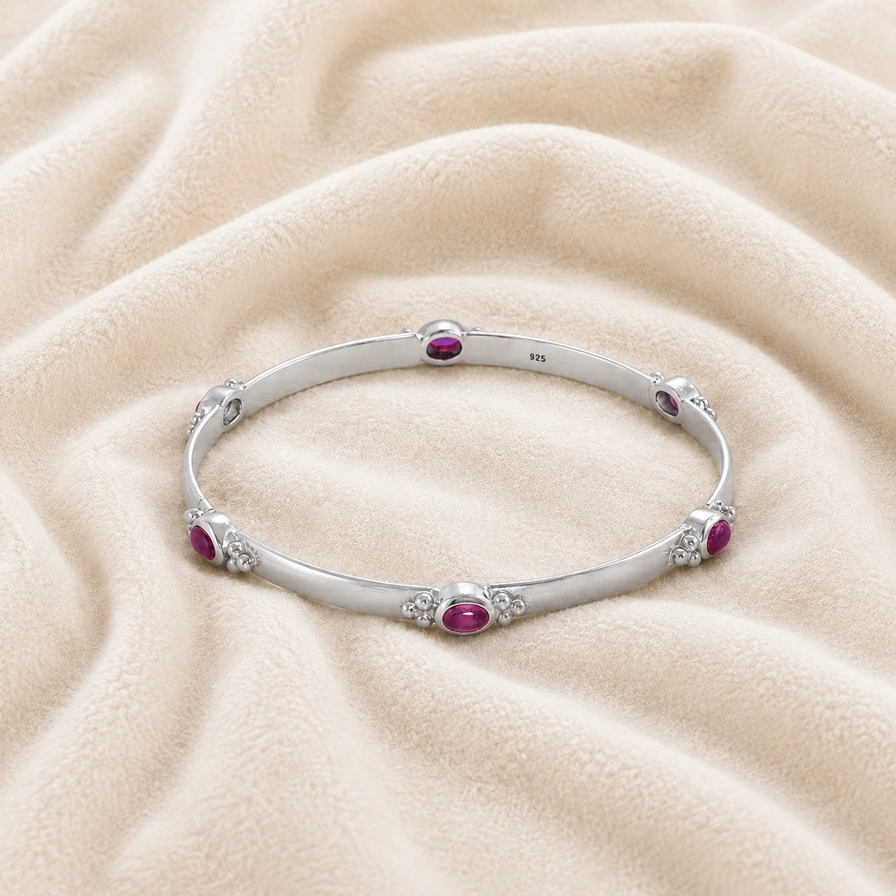 Amethyst_bracelet_in_sterling_silver_with_oval_amethyst_stones_at_front_angle_view_on_soft_fabric_background