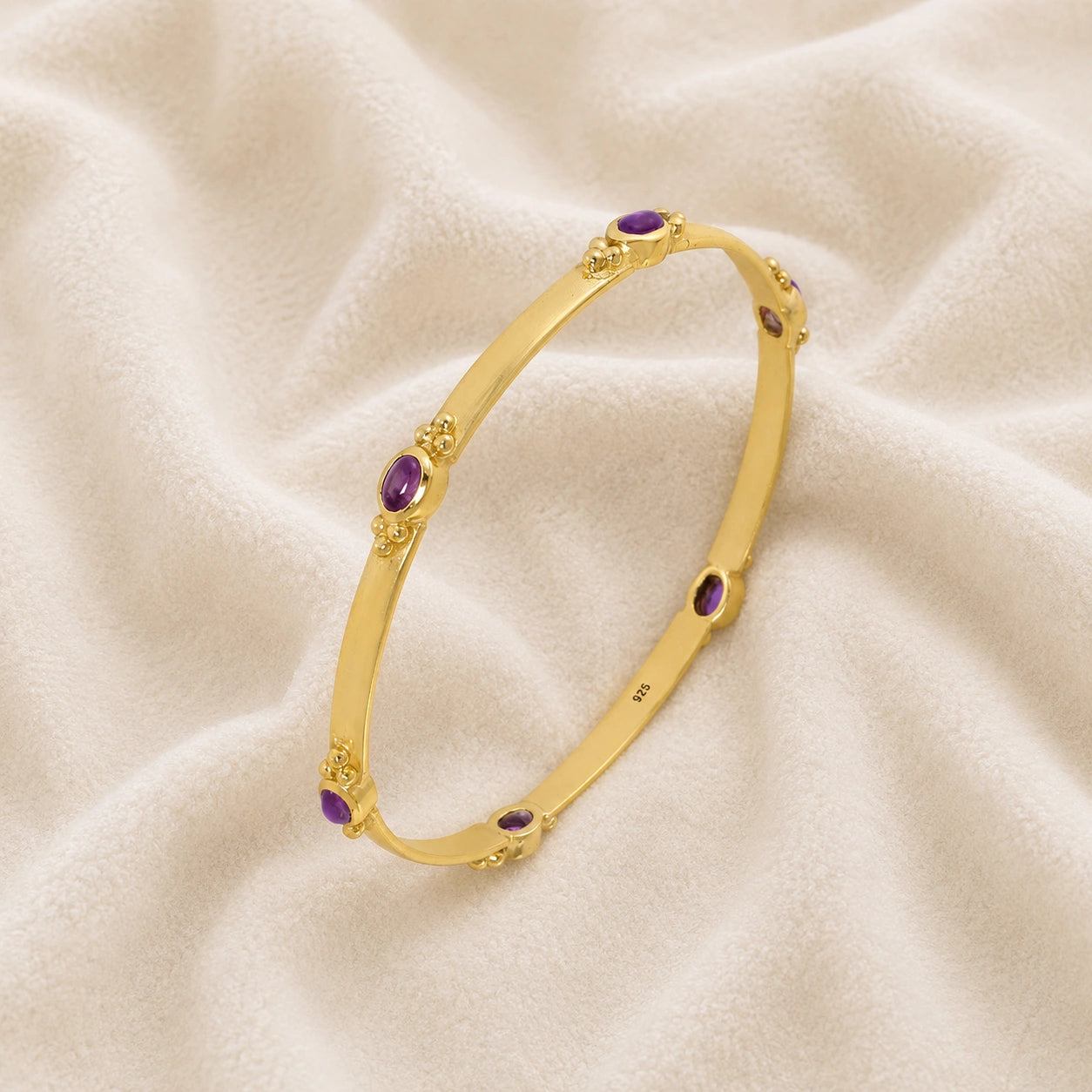 Amethyst_bracelet_in_gold_plated_silver_with_oval_amethyst_stones_at_slight_angle_view_on_soft_fabric_background