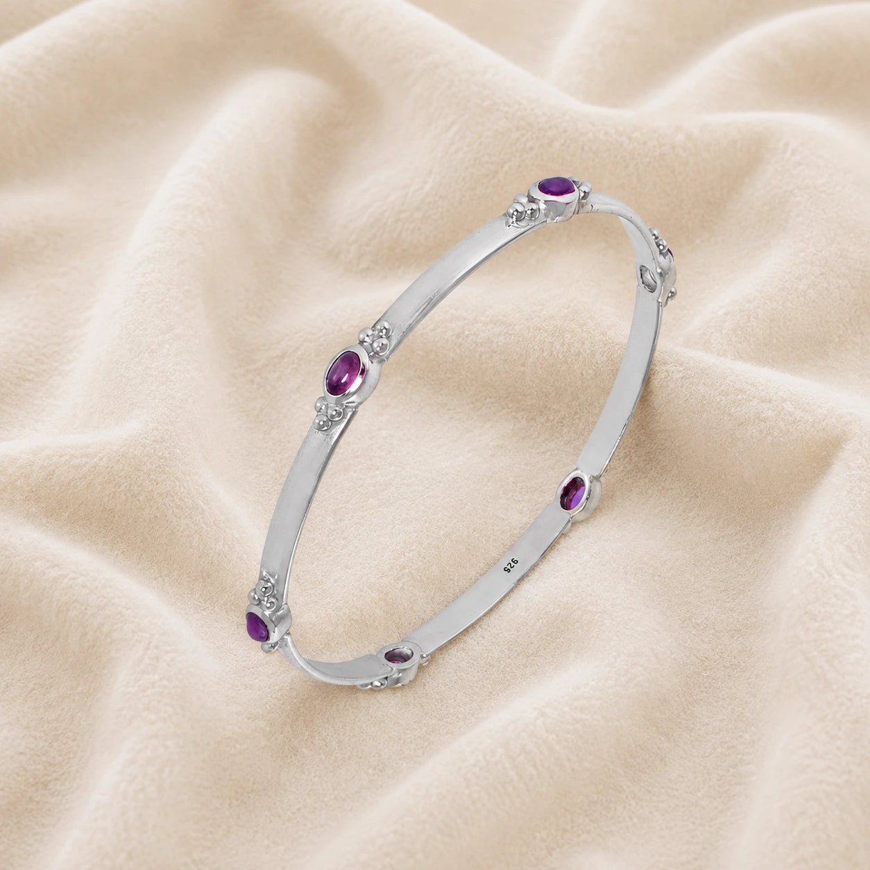 Amethyst_bracelet_in_sterling_silver_with_oval_amethyst_stones_at_slight_angle_view_on_soft_fabric_background