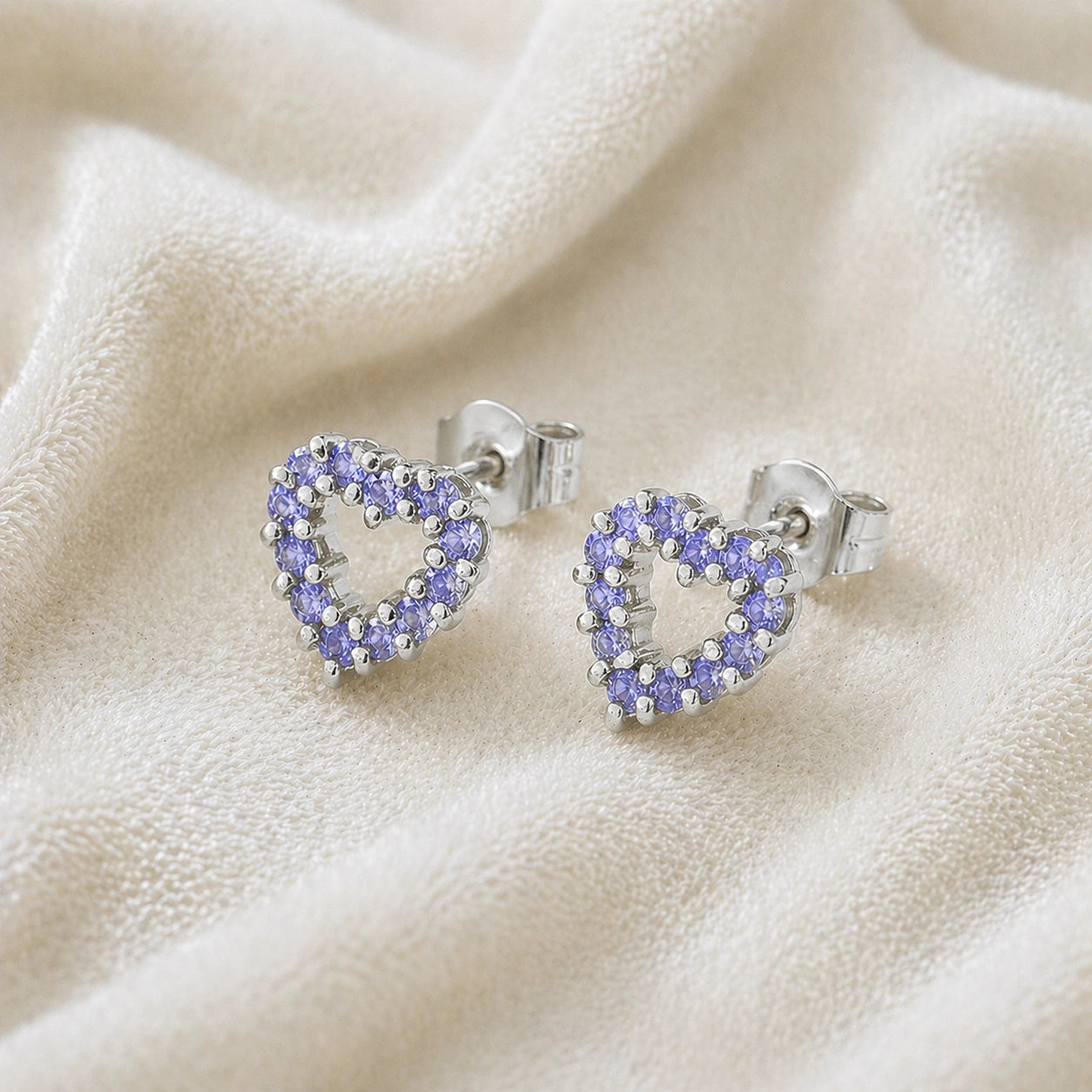 Amethyst_earrings_in_sterling_silver_heart_shape_with_amethyst_stones_at_a_slight_angle_view_on_soft_fabric_background