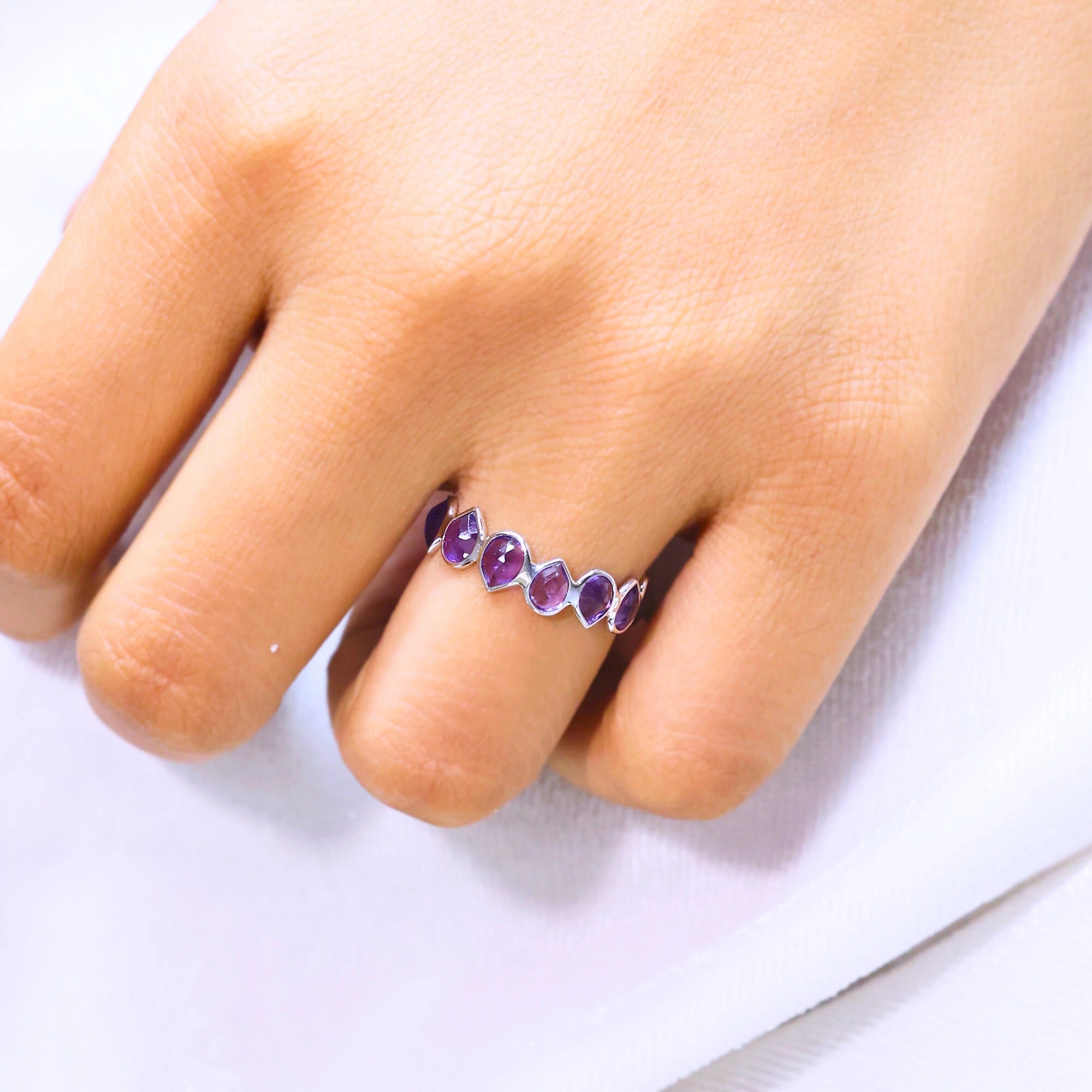 Angled close up shot of a hand wearing a sterling silver amethyst ring on a white cloth background with pear cut amethyst stones