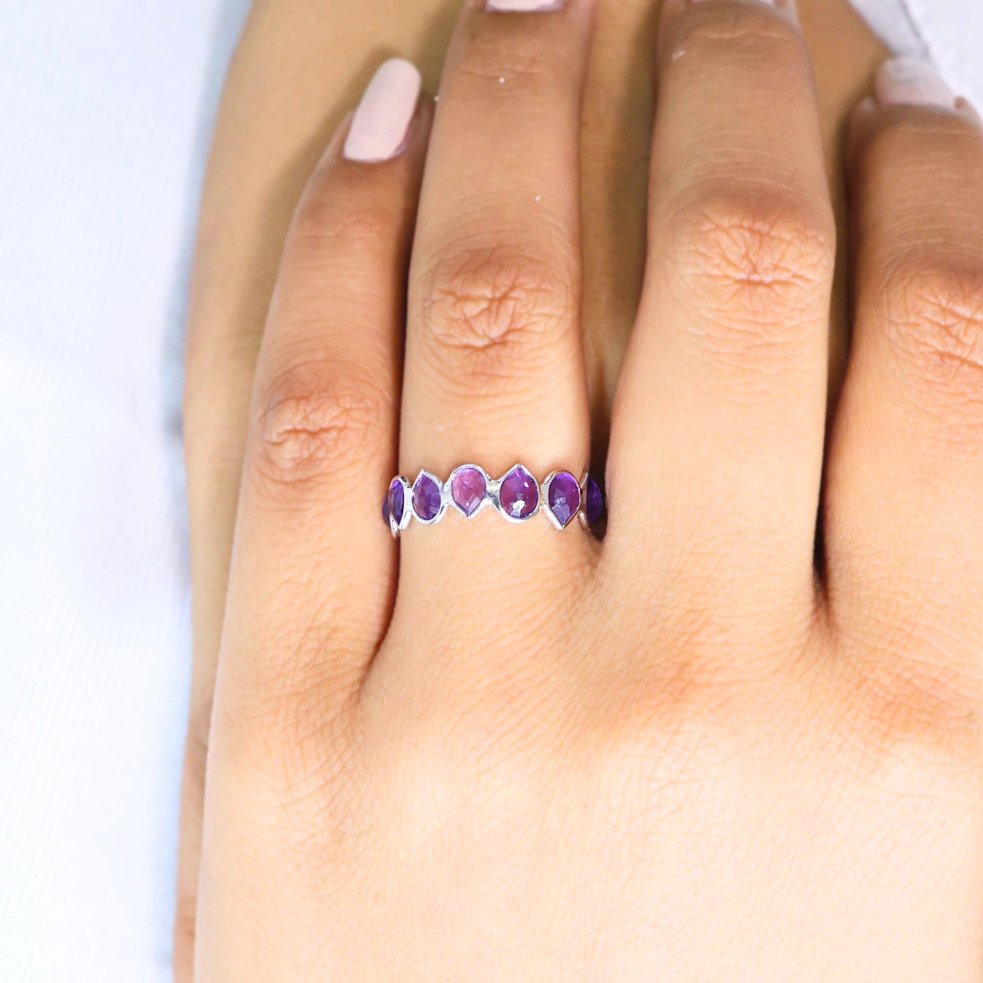 Angled close up shot of a hand wearing a sterling silver amethyst ring on a white background with pear cut amethyst stones