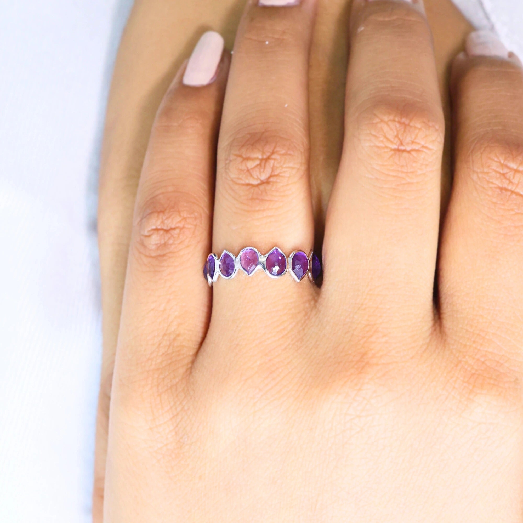 Angled close up shot of a hand wearing a sterling silver amethyst ring on a white background with pear cut amethyst stones