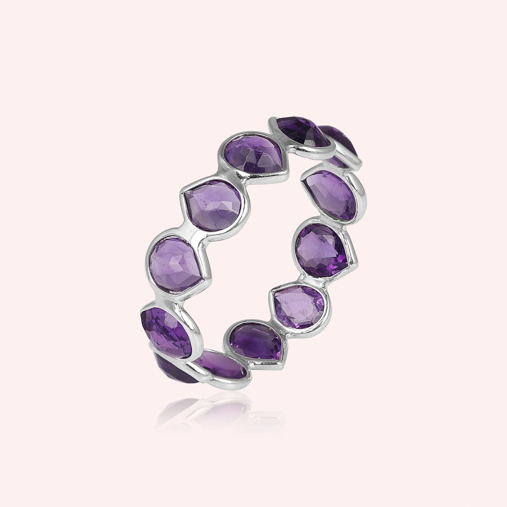 Angled shot of a sterling silver amethyst ring on a light pink background showcasing pear cut purple amethyst stones in a silver setting