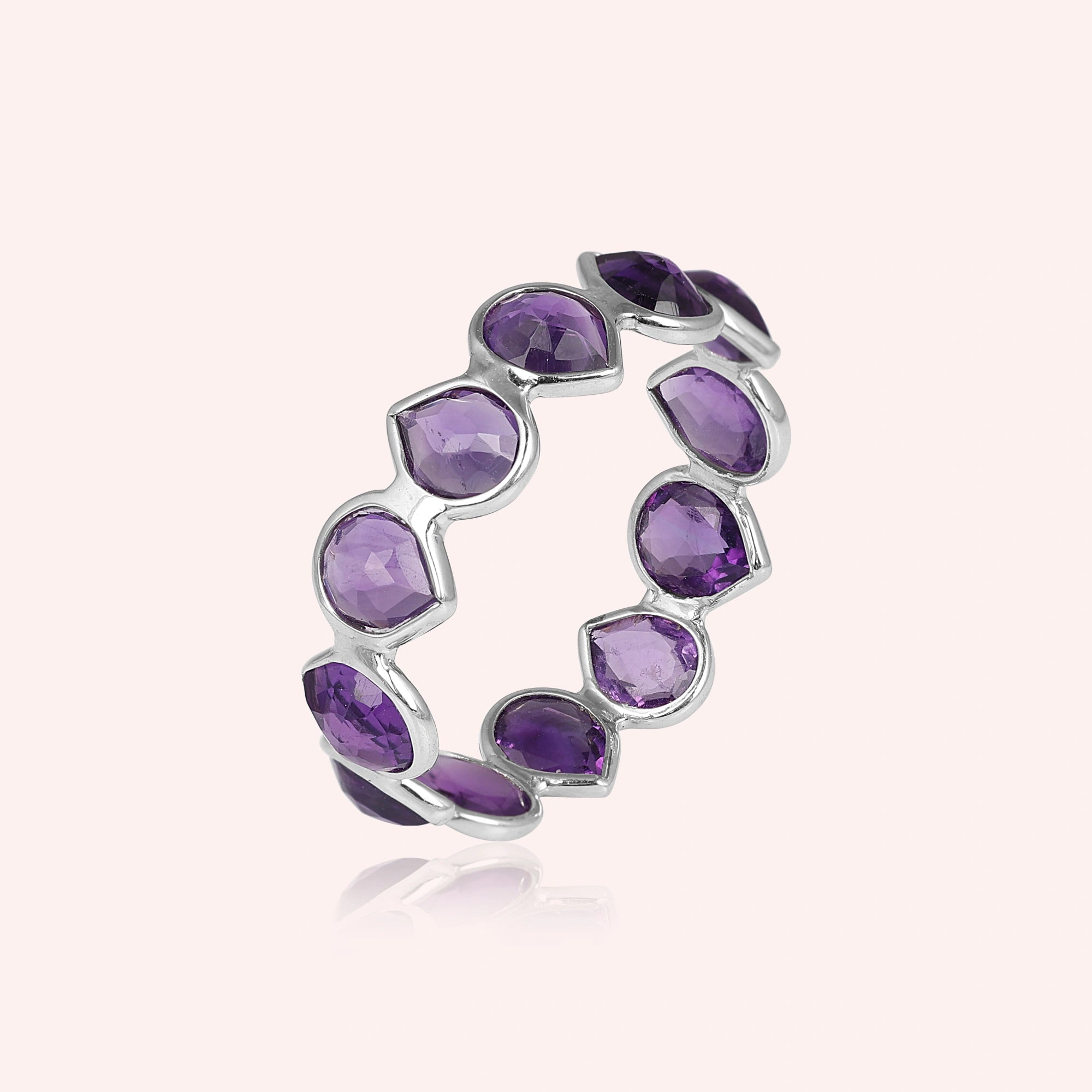 Angled shot of a sterling silver amethyst ring on a light pink background showcasing pear cut purple amethyst stones in a silver setting