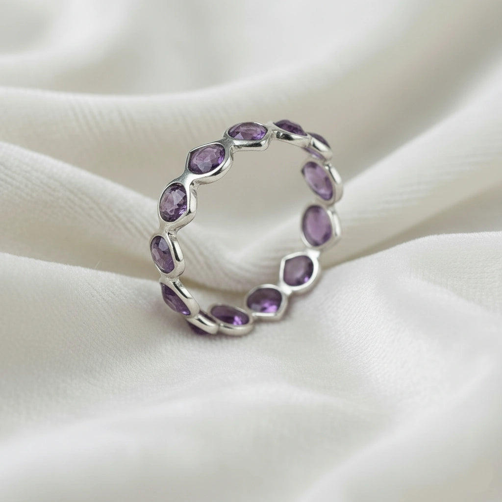 Angled close up shot of a sterling silver amethyst ring on a white velvet background showcasing oval cut purple amethyst stones