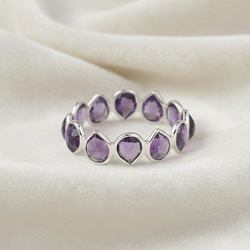 Horizontal close up shot of a sterling silver amethyst ring on a white cloth background with pear cut purple amethyst stones
