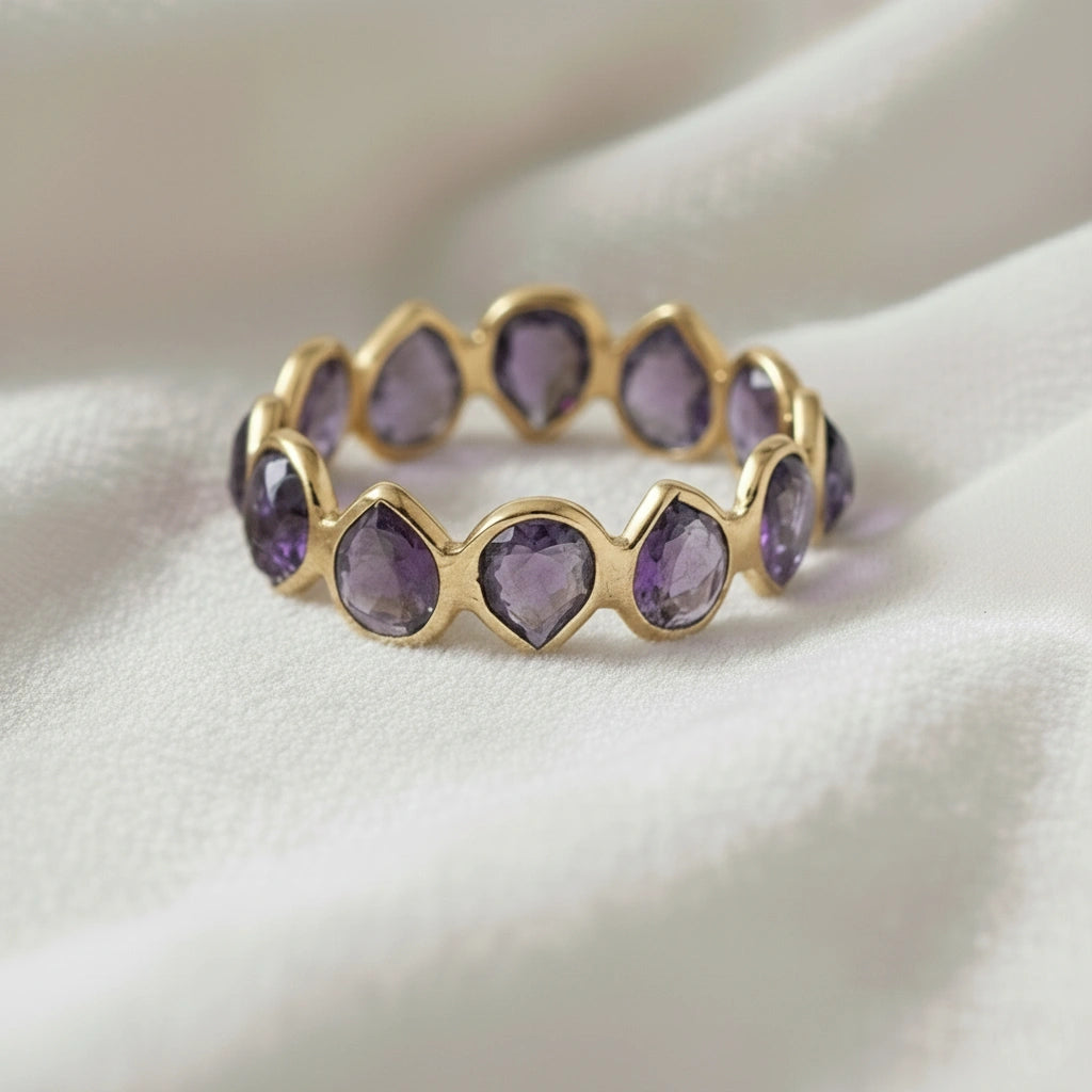 Horizontal close up shot of a gold-plated sterling silver amethyst ring on a white cloth with pear cut purple amethyst stones