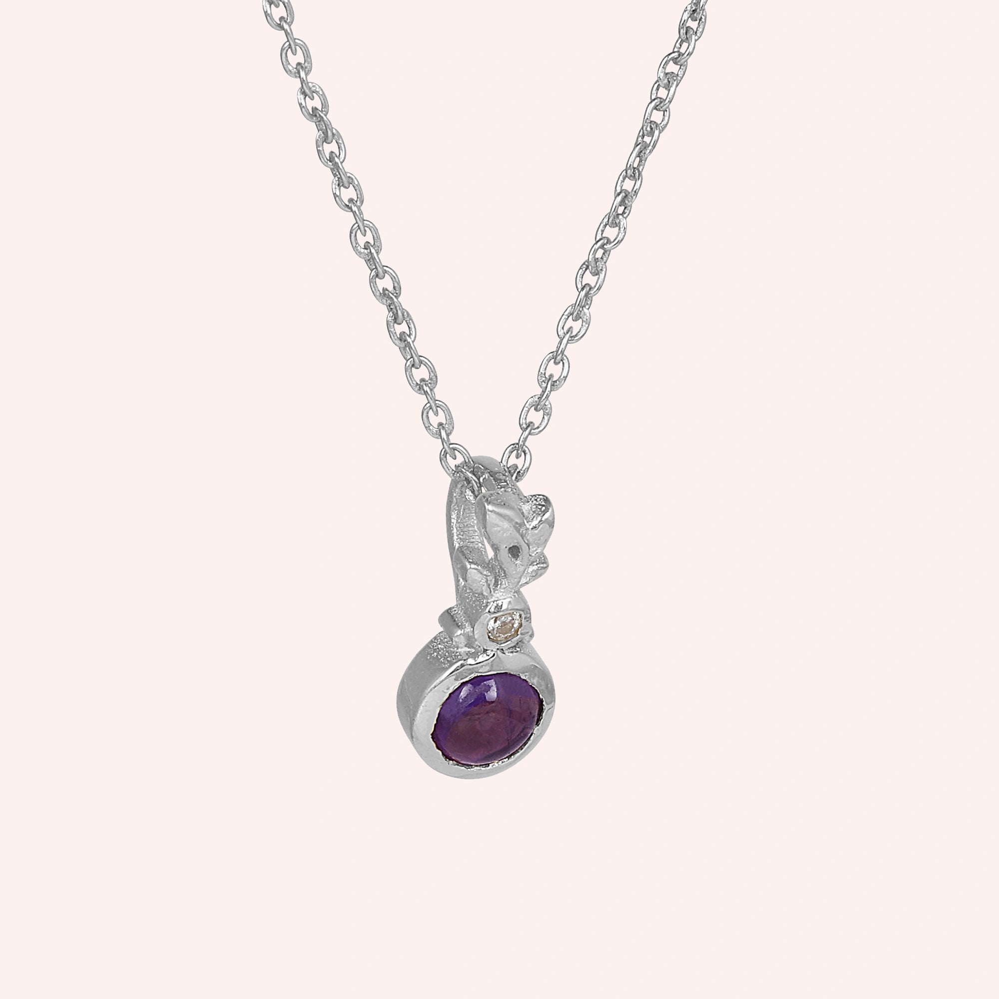 Amethyst_necklace_in_sterling_silver_with_amethyst_and_crystal_stones_at_slight_angle_view_on_solid_pink_background