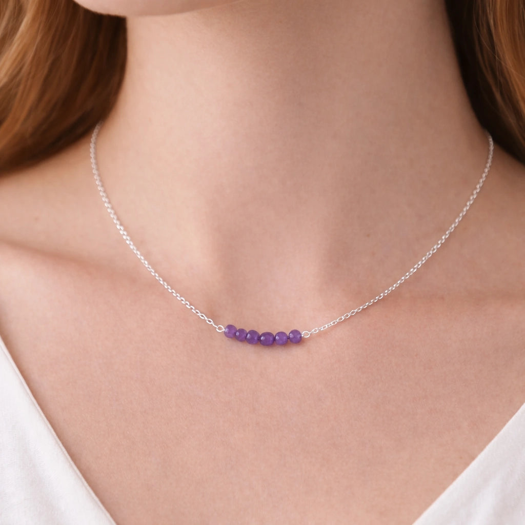 Angled_front_view_amethyst_necklace_with_purple_stone_beads_on_silver_chain_beaded_necklace_displayed_on_white_satin_fabric