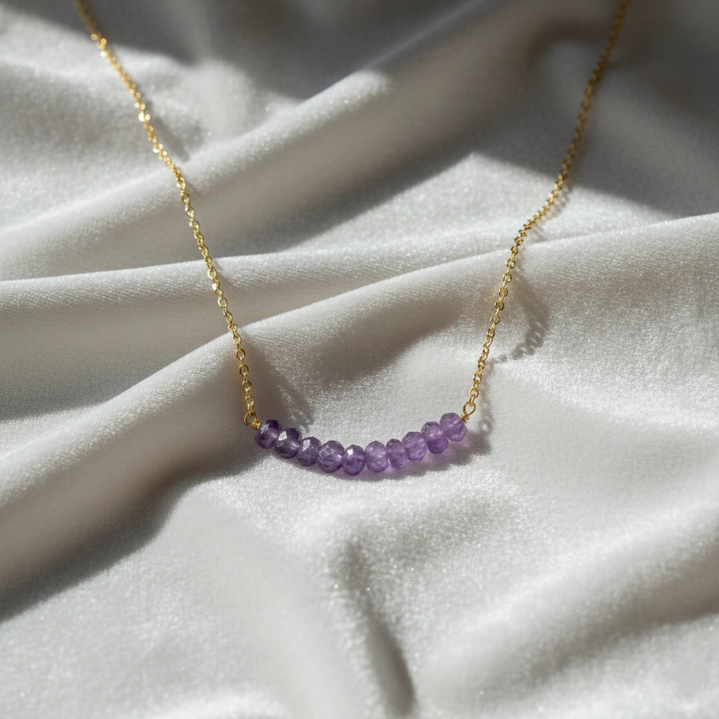 Angled_front_view_amethyst_necklace_with_purple_stone_beads_on_gold_plated_chain_beaded_necklace_displayed_on_white_satin_fabric