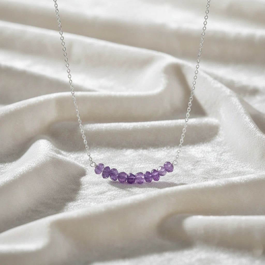 Angled_front_view_amethyst_necklace_with_purple_stone_beads_on_silver_chain_beaded_necklace_displayed_on_white_satin_fabric