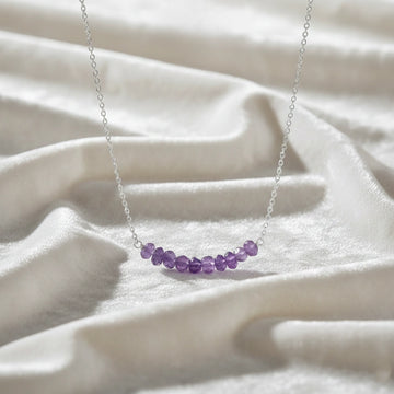 Angled_front_view_amethyst_necklace_with_purple_stone_beads_on_silver_chain_beaded_necklace_displayed_on_white_satin_fabric