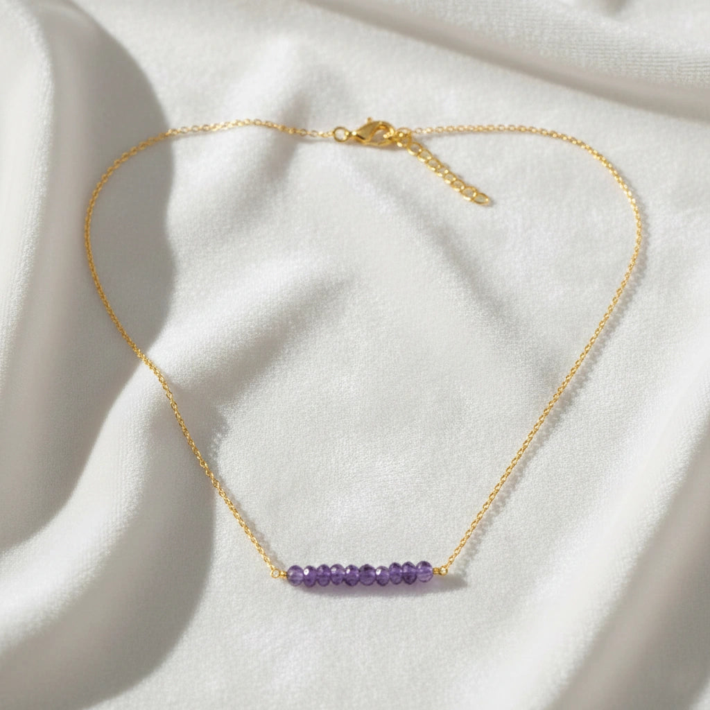 Angled_front_view_amethyst_necklace_with_purple_beads_on_gold_plated_chain_beaded_necklace_on_white_satin_fabric_background