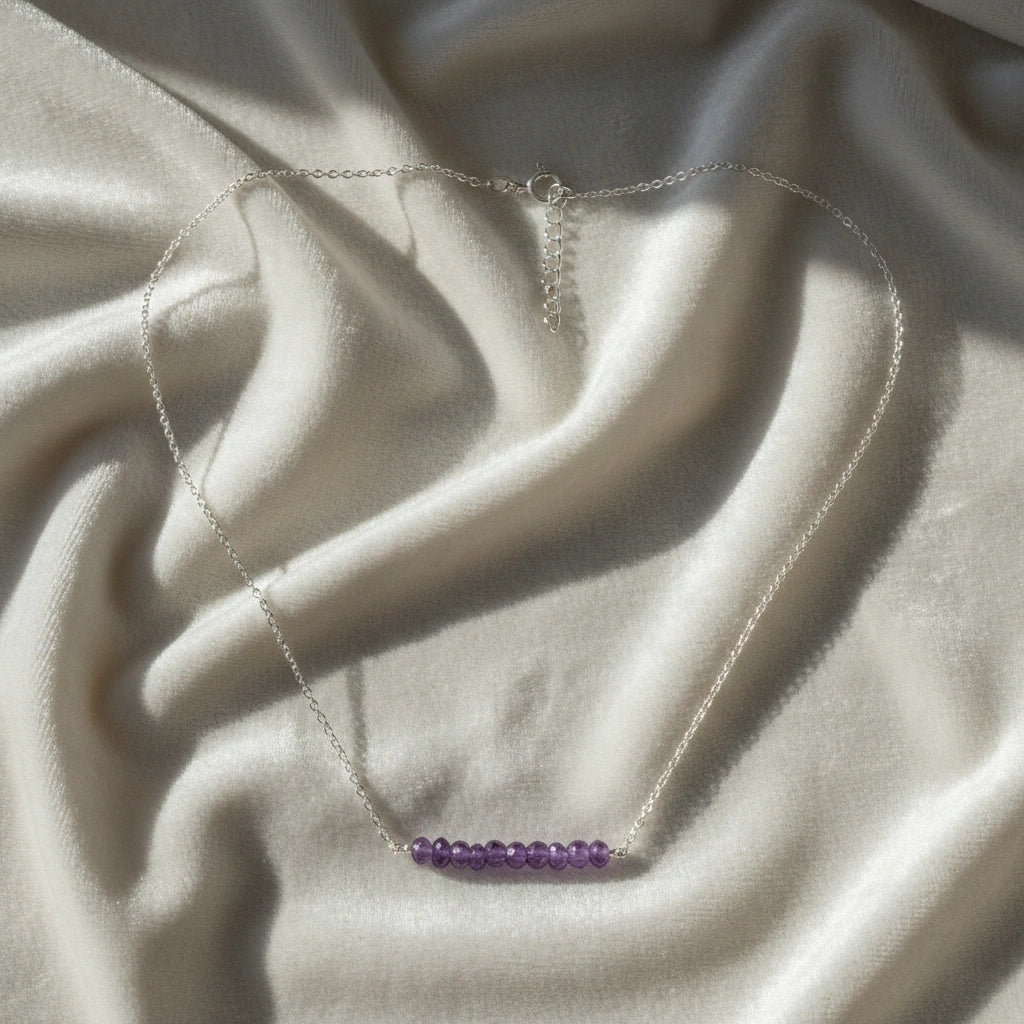 Angled_front_view_amethyst_necklace_with_purple_beads_on_silver_chain_beaded_necklace_on_white_satin_fabric_soft_background