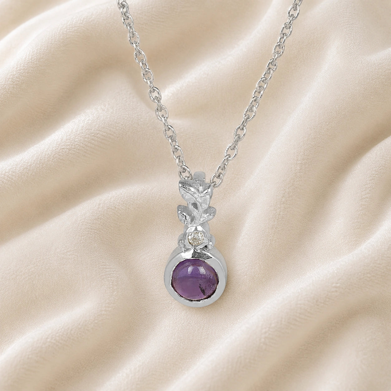Amethyst_necklace_in_sterling_silver_with_amethyst_and_crystal_stones_at_front_angle_view_on_soft_fabric_background