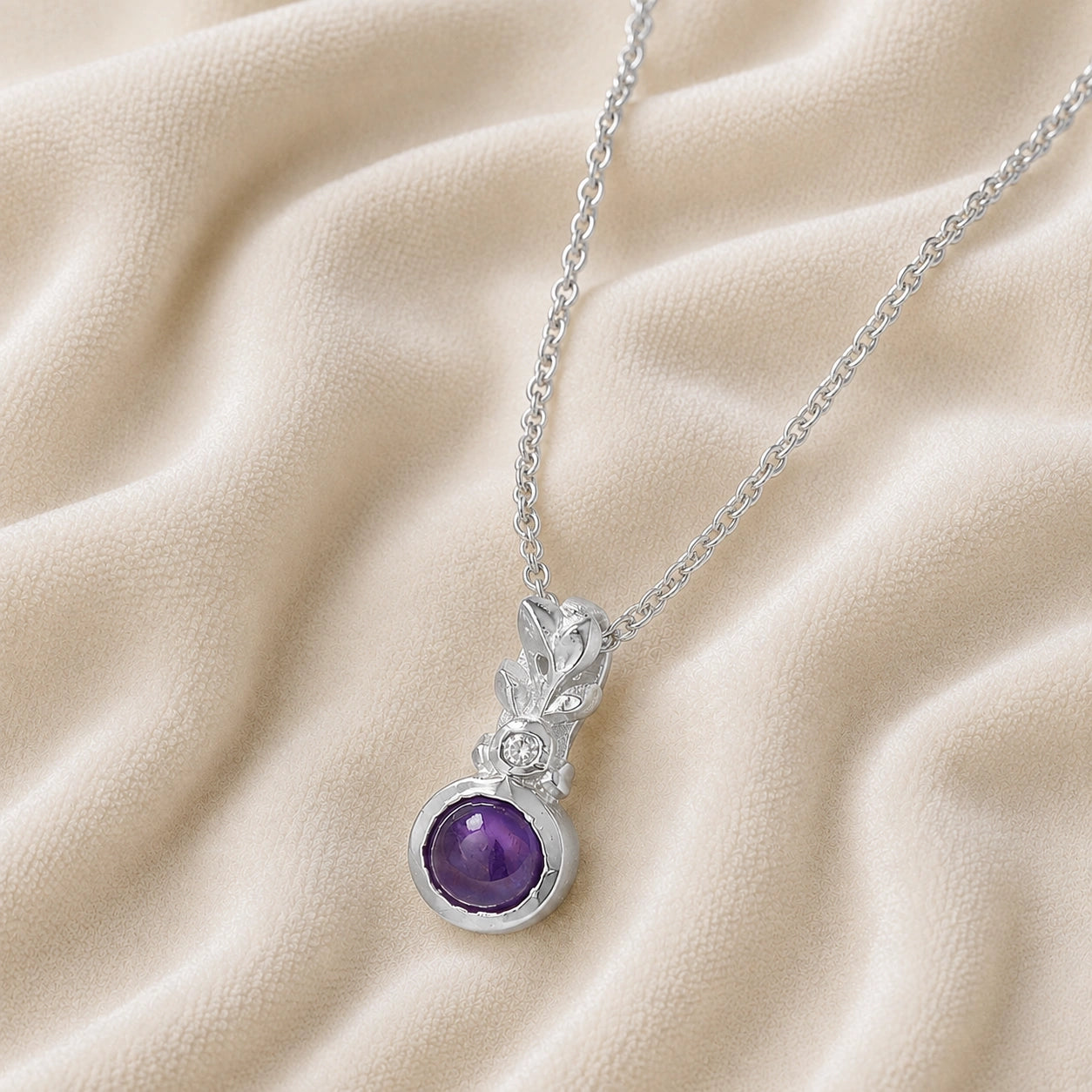 Amethyst_necklace_in_sterling_silver_with_amethyst_and_crystal_stones_at_slight_angle_view_on_soft_fabric_background