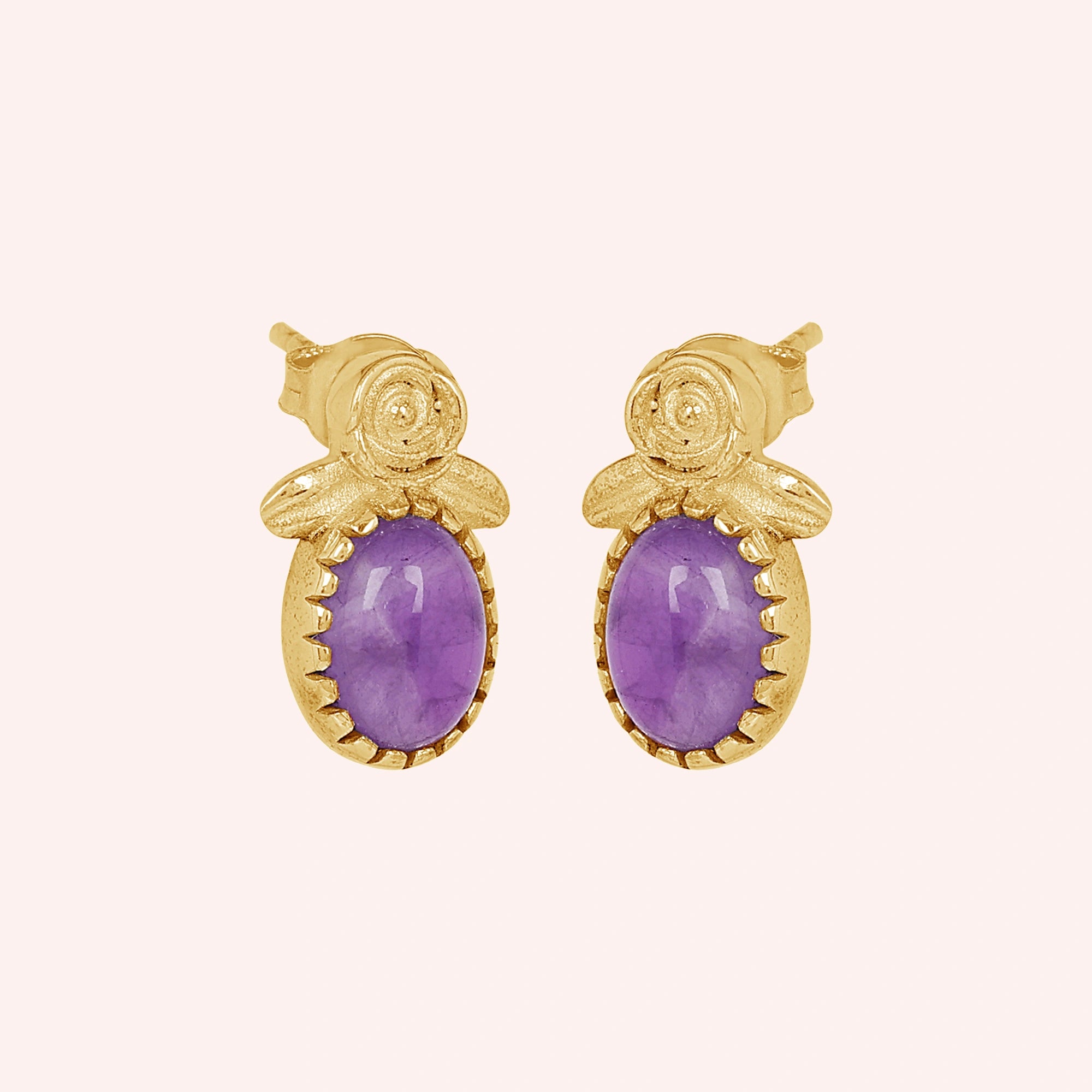 Front_view_amethyst_stud_earrings_with_oval_purple_gemstone_in_gold_plated_flower_stud_earrings_on_soft_pink_background