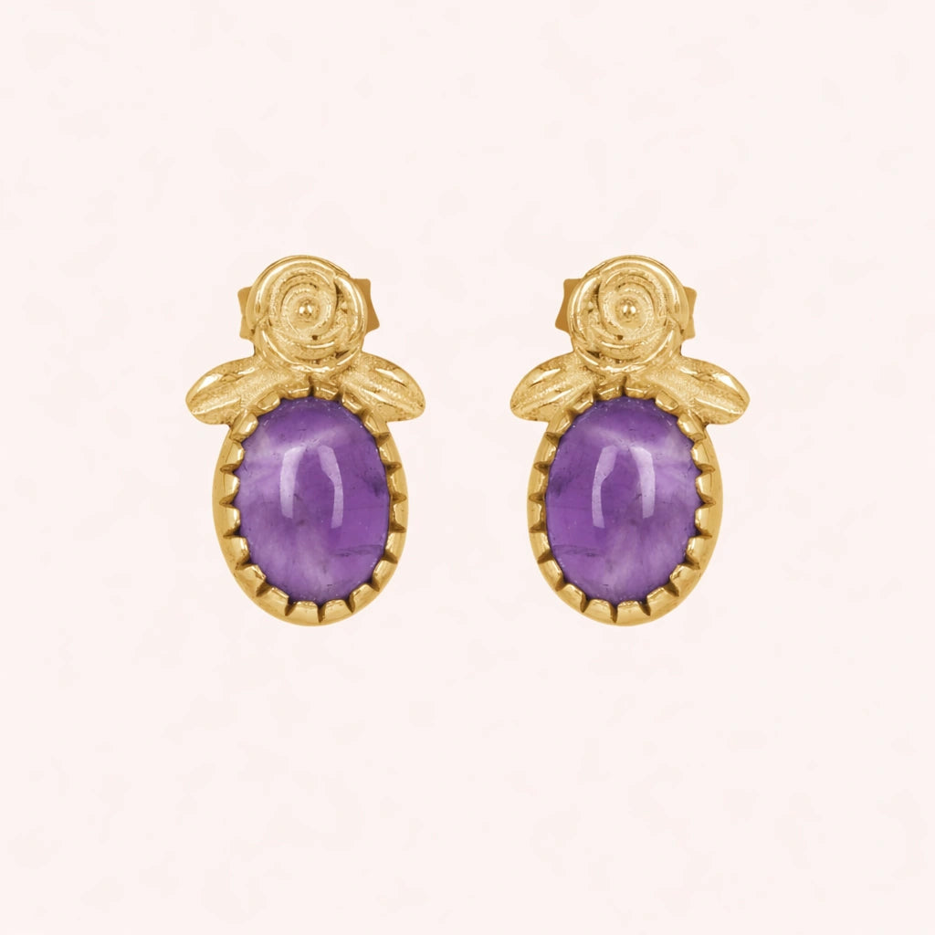 Front_view_amethyst_stud_earrings_with_oval_purple_gemstone_set_in_gold_plated_flower_stud_earrings_on_soft_pink_background