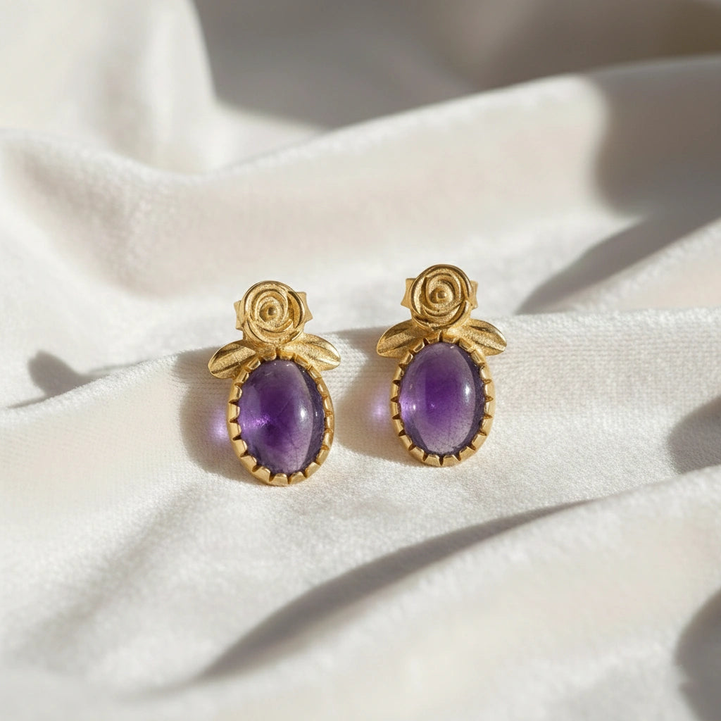Front_view_amethyst_stud_earrings_with_oval_purple_gemstone_set_in_gold_plated_flower_stud_earrings_on_white_fabric_background
