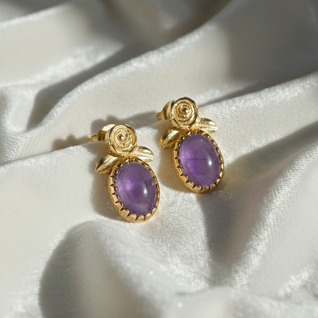 Angled_front_view_amethyst_stud_earrings_with_oval_purple_gemstone_set_in_gold_plated_flower_stud_earrings_on_white_fabric