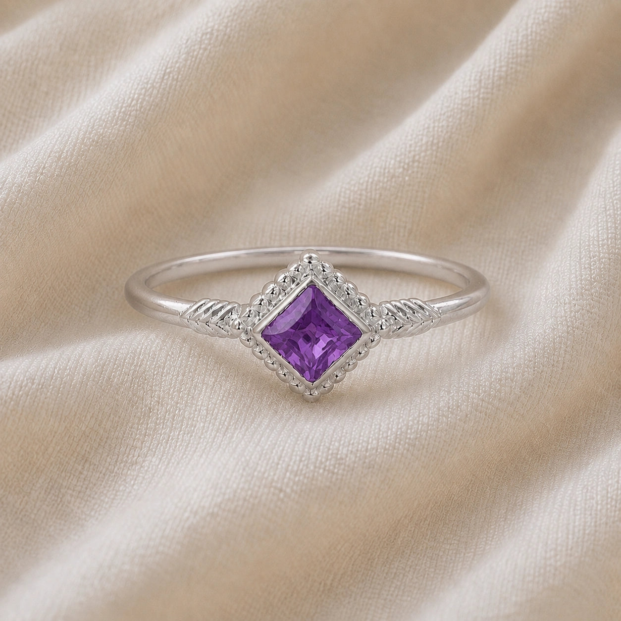 Princess_cut_ring_sterling_silver_with_square_amethyst_and_detailed_band_front_angle_view_on_soft_fabric_background
