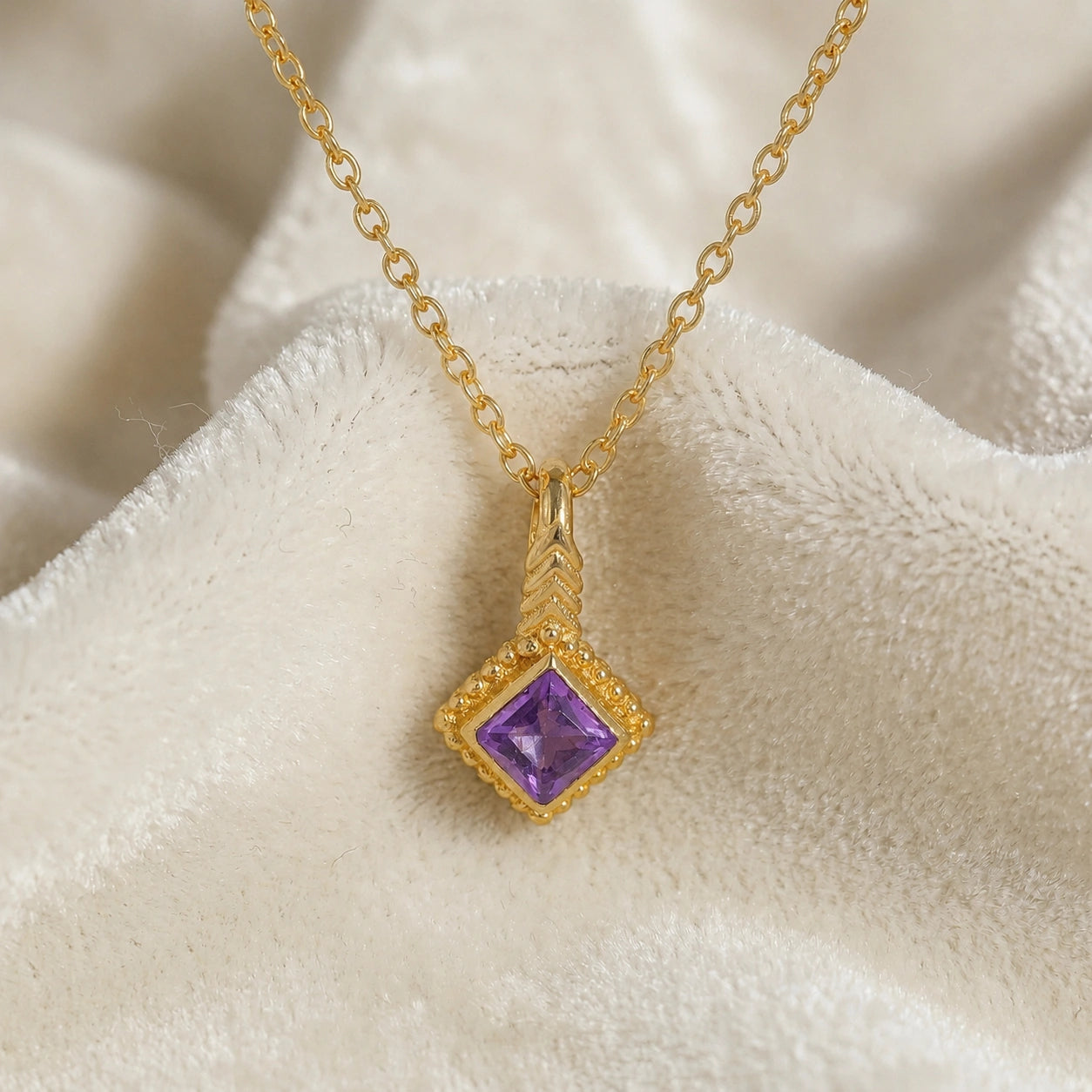 Birthstone_necklace_in_gold_plated_silver_with_square_cut_amethyst_pendant_in_front_angle_view_on_soft_white_fabric_background